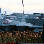 Trump salutes in front of a large military aircraft, symbolizing his alignment with military power. This image visually represents the article's theme of a potential Trump-led military intervention in Venezuela amidst a domestic political crisis.